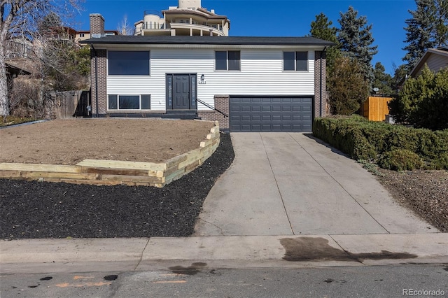 split foyer home with a garage, driveway, brick siding, and fence