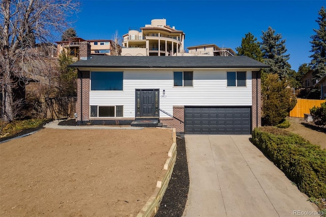 split foyer home with driveway, brick siding, an attached garage, and fence