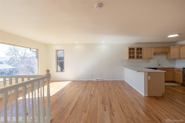 kitchen featuring a peninsula, a sink, light countertops, light wood finished floors, and tasteful backsplash