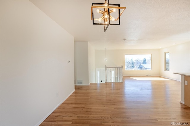 unfurnished room with baseboards, an inviting chandelier, visible vents, and light wood-style floors