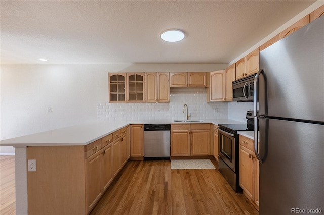 kitchen with a peninsula, light wood finished floors, stainless steel appliances, and light brown cabinetry