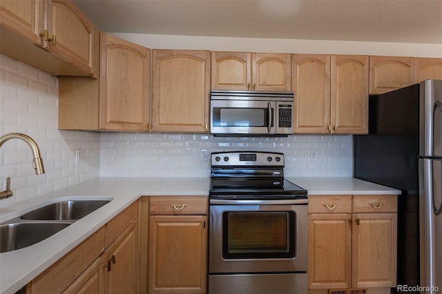 kitchen featuring light brown cabinets, stainless steel appliances, a sink, light countertops, and backsplash