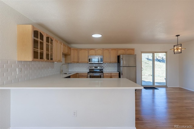 kitchen with stainless steel appliances, light countertops, backsplash, glass insert cabinets, and wood finished floors