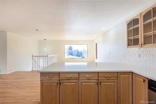 kitchen featuring glass insert cabinets, a peninsula, light countertops, a textured ceiling, and stainless steel dishwasher