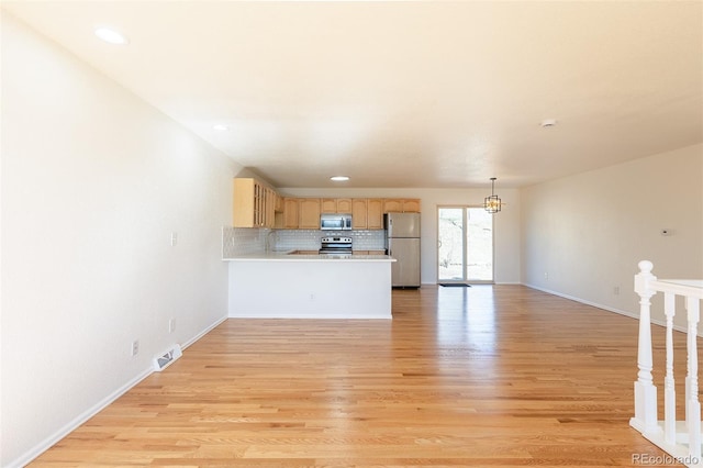 kitchen with a peninsula, appliances with stainless steel finishes, light wood-type flooring, and light countertops