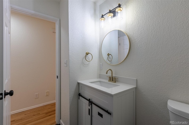 bathroom featuring a textured wall, toilet, vanity, wood finished floors, and baseboards