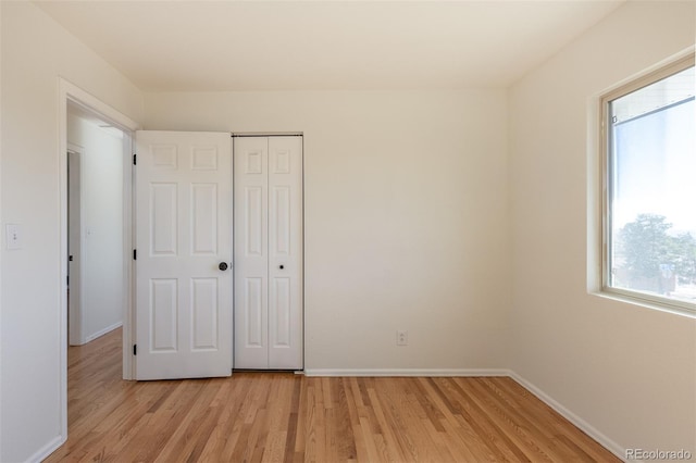 unfurnished bedroom featuring light wood-style floors, baseboards, and a closet