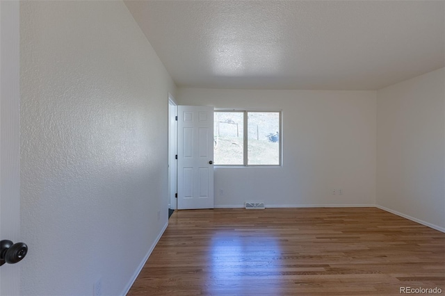 unfurnished room featuring a textured ceiling, a textured wall, wood finished floors, visible vents, and baseboards