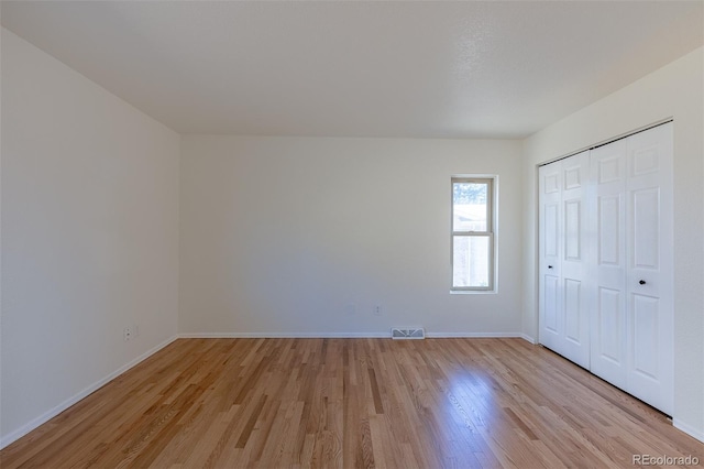 unfurnished bedroom with a closet, light wood-type flooring, visible vents, and baseboards