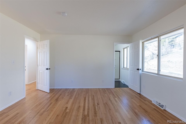 spare room featuring light wood-type flooring, visible vents, and baseboards