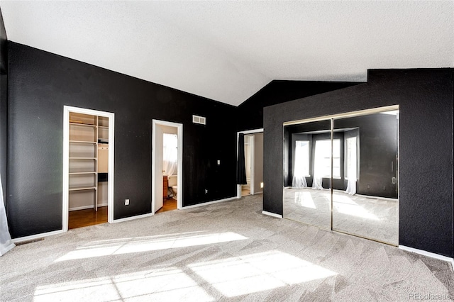 unfurnished bedroom with lofted ceiling, carpet, a walk in closet, and ensuite bath