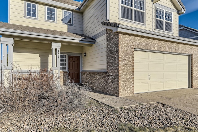 doorway to property featuring brick siding, an attached garage, and concrete driveway