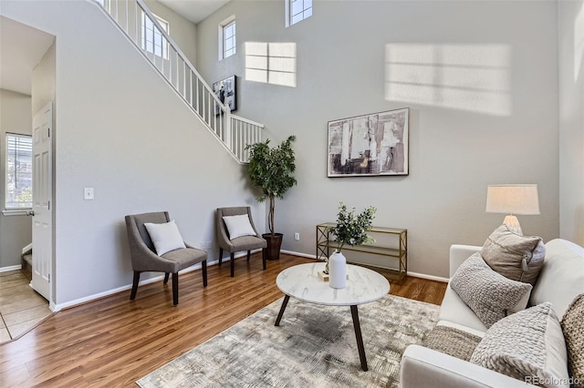 living room with a wealth of natural light, baseboards, wood finished floors, and a towering ceiling