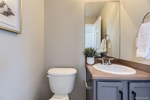 half bath featuring toilet, vanity, and a textured wall