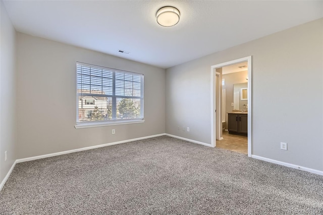 unfurnished bedroom with visible vents, connected bathroom, baseboards, carpet, and a sink