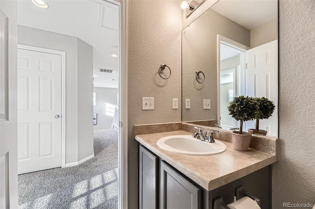 bathroom featuring vanity, a textured wall, visible vents, and baseboards