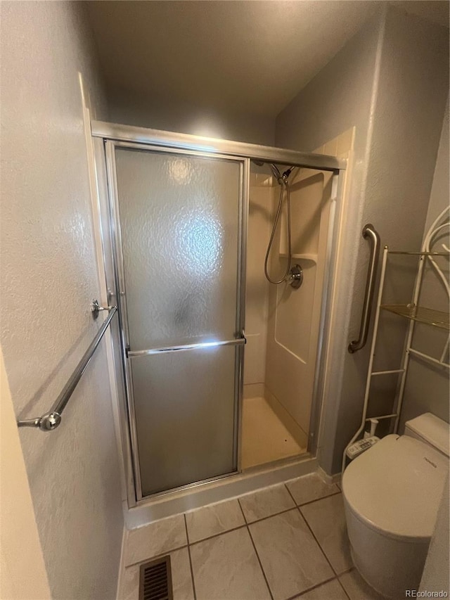 bathroom featuring tile patterned flooring, toilet, and a shower with door