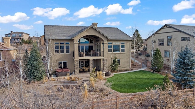 back of house with a lawn, a balcony, and a hot tub