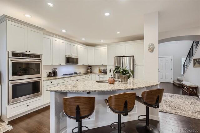 kitchen featuring sink, stainless steel appliances, a kitchen breakfast bar, light stone countertops, and dark hardwood / wood-style flooring