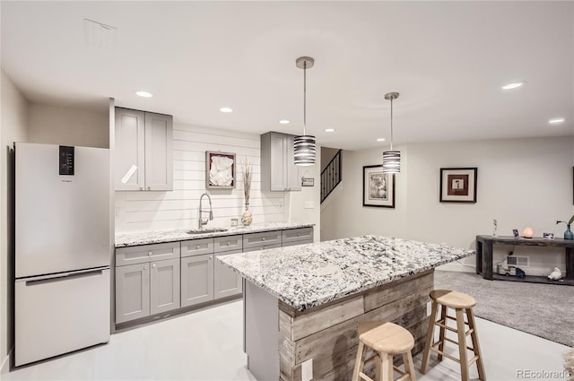 kitchen featuring decorative light fixtures, sink, gray cabinetry, white refrigerator, and light stone countertops