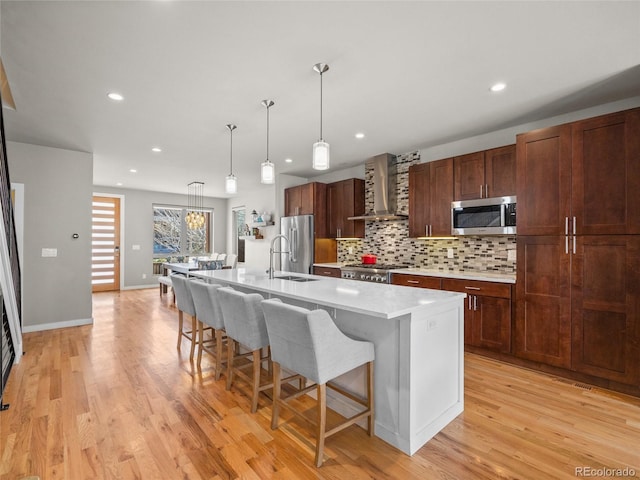 kitchen with a sink, wall chimney range hood, stainless steel appliances, light countertops, and decorative backsplash