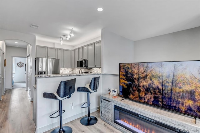 837 E 98th Ave Unit 403, Thornton, CO 80229 - kitchen with appliances with stainless steel finishes, gray cabinetry, arched walkways, light wood-type flooring, and light stone counters