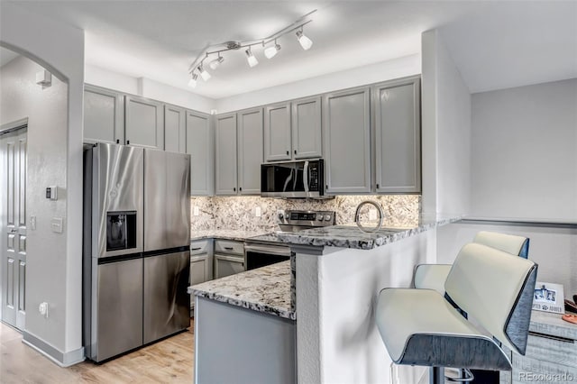 837 E 98th Ave Unit 403, Thornton, CO 80229 - kitchen featuring stainless steel appliances, gray cabinetry, a peninsula, light stone countertops, and light wood finished floors