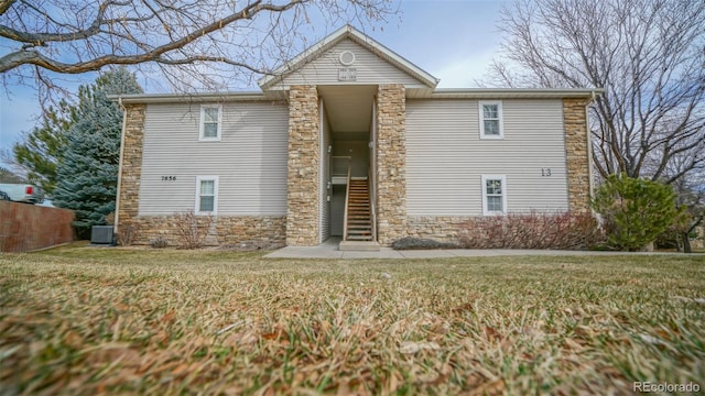 traditional-style house featuring stone siding, central AC unit, and a front lawn