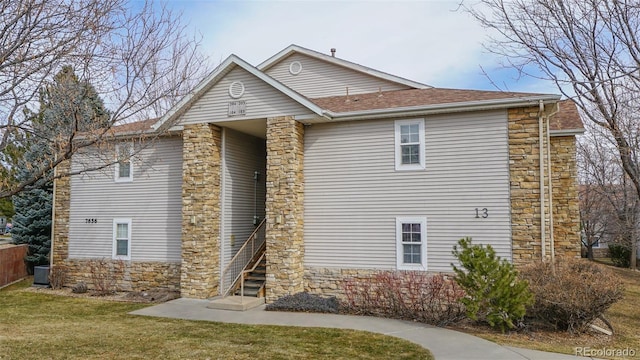view of front facade with central AC, roof with shingles, stone siding, and a front yard