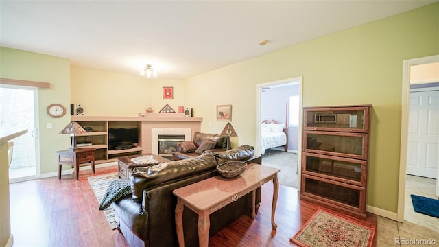 living area with a tile fireplace, plenty of natural light, wood finished floors, and baseboards