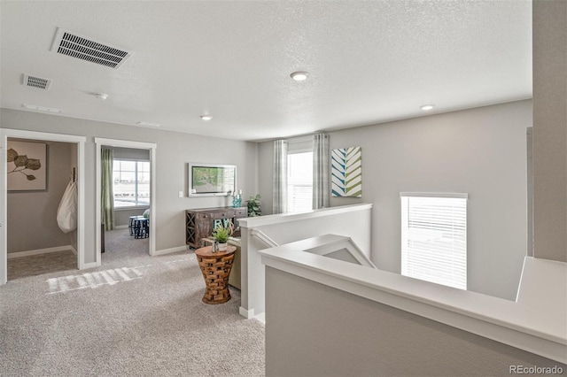 corridor with a textured ceiling and light colored carpet