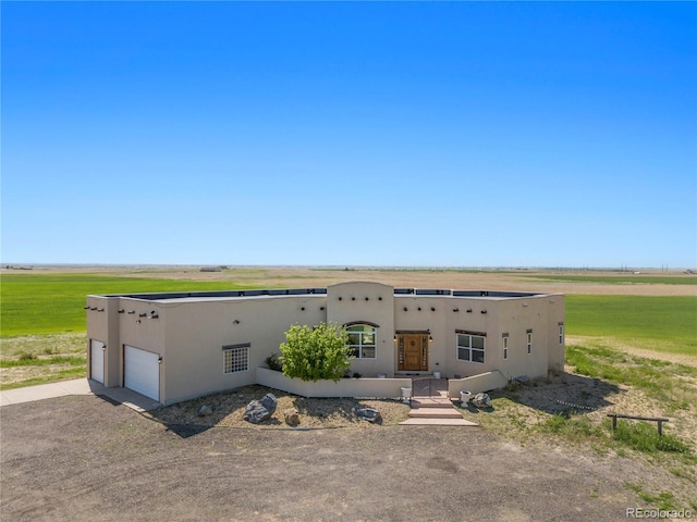 pueblo revival-style home featuring a front lawn, a rural view, and a garage