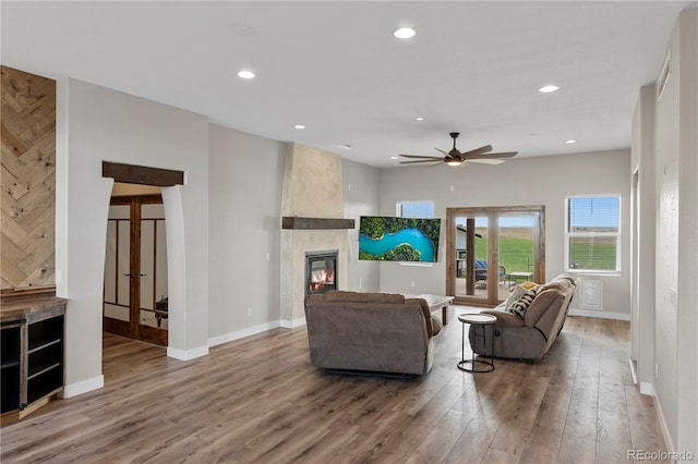 living room featuring ceiling fan, a large fireplace, and wood-type flooring