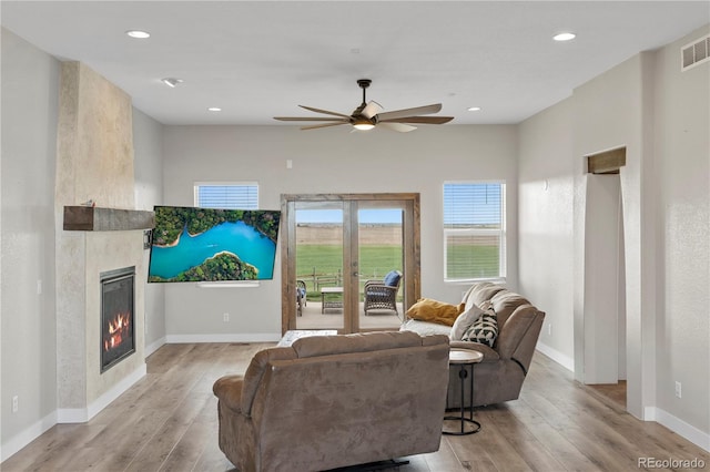 living room featuring a large fireplace, ceiling fan, light hardwood / wood-style floors, and french doors