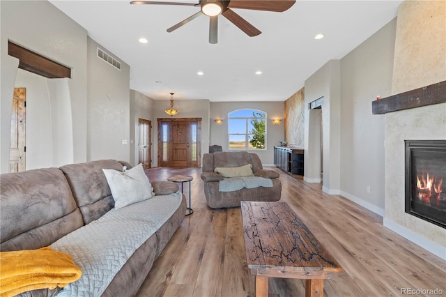 living room featuring a tile fireplace, light hardwood / wood-style floors, and ceiling fan