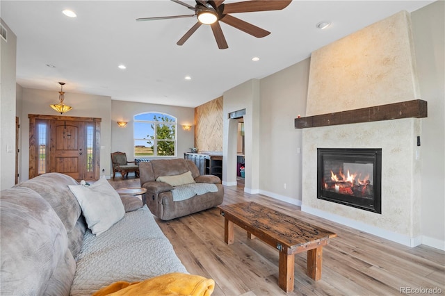 living room featuring a large fireplace, light hardwood / wood-style floors, and ceiling fan