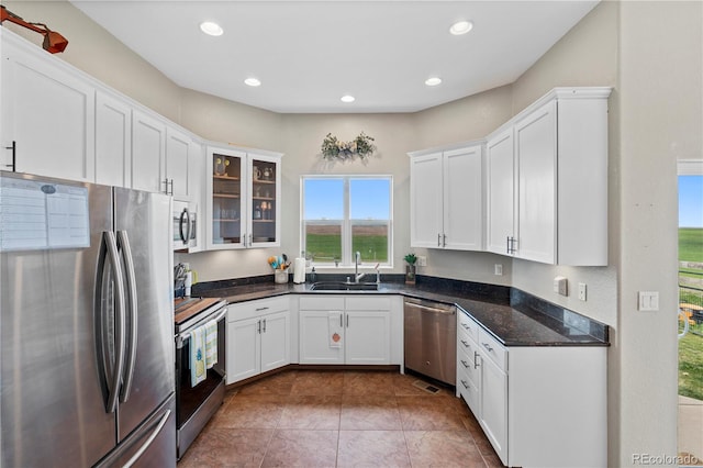 kitchen with sink, tile patterned flooring, dark stone countertops, appliances with stainless steel finishes, and white cabinetry