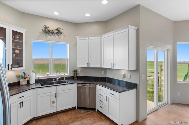 kitchen featuring stainless steel dishwasher, white cabinets, sink, and dark stone counters