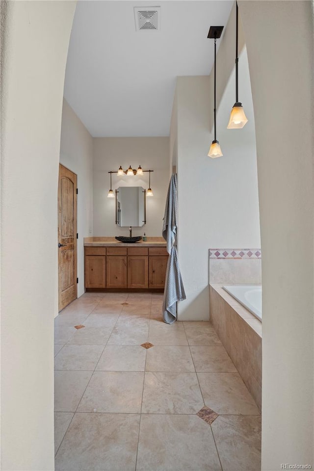 bathroom with tile patterned flooring, vanity, and a relaxing tiled tub