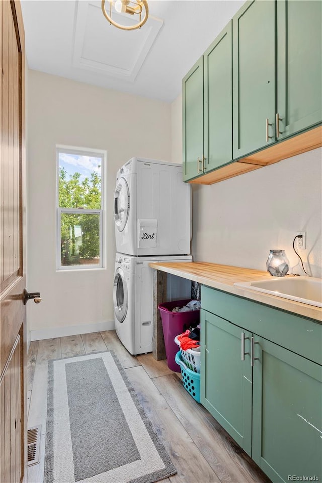 clothes washing area with stacked washing maching and dryer, sink, cabinets, and light hardwood / wood-style floors