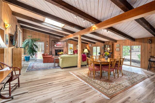 dining room featuring a brick fireplace, lofted ceiling with skylight, light wood-type flooring, and wood walls