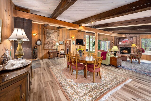 dining space with wooden walls, lofted ceiling with beams, light wood-type flooring, and a brick fireplace