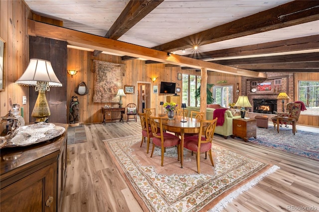 dining space with light wood-type flooring, wood walls, beamed ceiling, and a brick fireplace