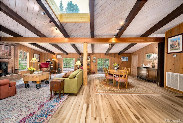 living room featuring wood walls, plenty of natural light, light hardwood / wood-style floors, and lofted ceiling with skylight