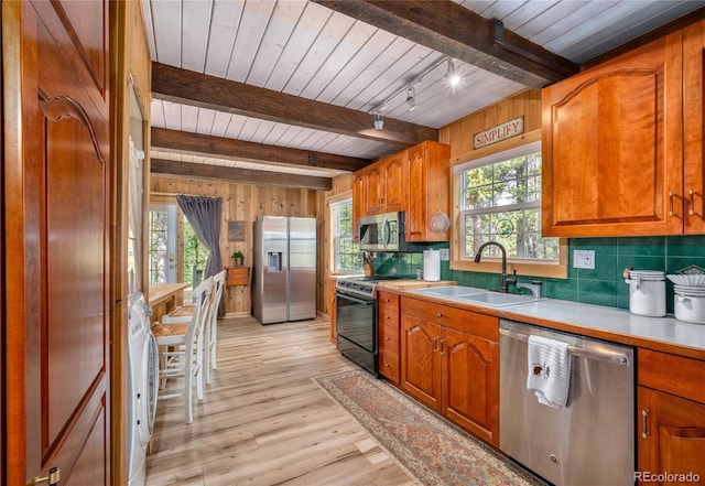 kitchen with a healthy amount of sunlight, appliances with stainless steel finishes, beam ceiling, and light hardwood / wood-style flooring