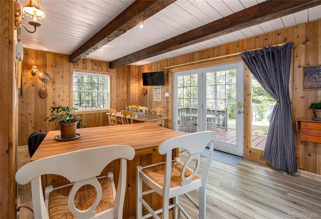 dining space with wooden ceiling, wood walls, light wood-style floors, and beam ceiling