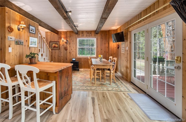 dining room featuring light wood-style flooring, wood walls, stairs, beamed ceiling, and track lighting