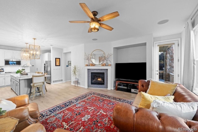 10837 Fox Sedge Way, Highlands Ranch, CO 80126 - living area with light wood-style flooring, ceiling fan, a chandelier, and a brick fireplace