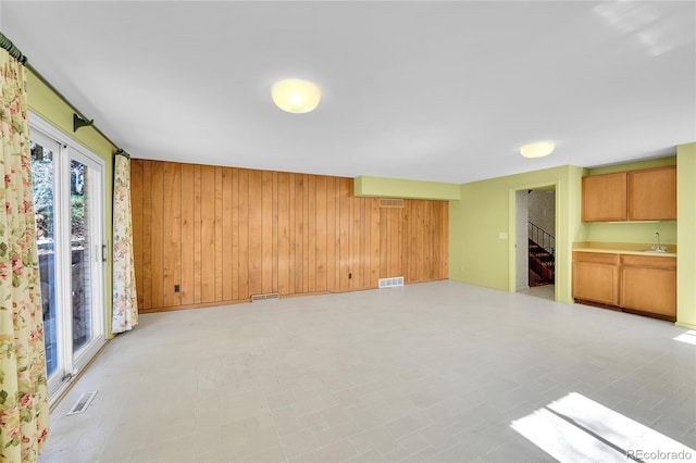 unfurnished living room with a sink, visible vents, wood walls, and stairway