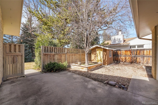 view of patio with an outdoor structure, a garden, a fenced backyard, and a shed